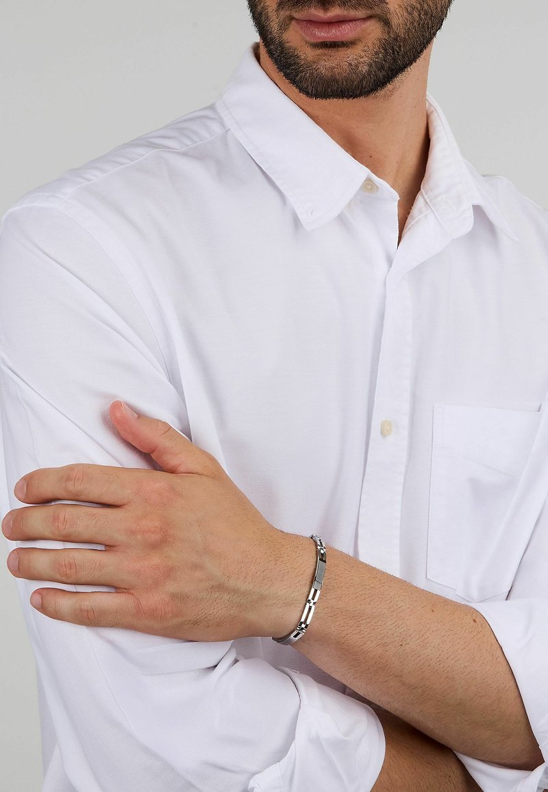 Bracciale in acciaio inossidabile con link intrecciati, con una finitura lucida e una leggera texture, indossato al polso di un uomo.