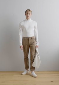 Suéter de cuello alto blanco, pantalones de pana beige y zapatillas blancas. Un chal gris claro drapeado sobre un brazo. Diseño y texturas sencillas y ajustadas.
