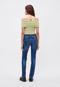 Zeleni kratki top brez ramen z rebrasto teksturo in modre kavbojke iz jeansa. Kavbojke imajo žep na zadnji strani in rjav usnjen detajl.