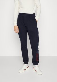 Dark blue sweatpants made of cotton blend, featuring an elastic waistband and cuffs, with red and blue branding on the left leg.