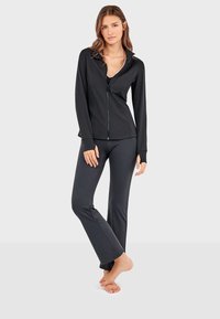Ensemble de vêtements de sport noir comprenant une veste zippée avec col et manches longues, associée à un pantalon ajusté. Tissu lisse et extensible.