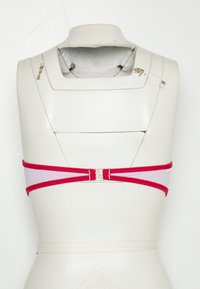 Rød og hvit stoff-BH med et enkelt design, som har et smalt bånd, justerbare stropper og en metallspenne bak.