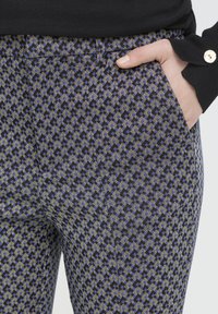 Gemusterte Hosen mit einem lila, blauen und gelben Webdesign. Verfügen über Seitentaschen und eine taillierte Passform, hergestellt aus einem strukturierten Stoff.