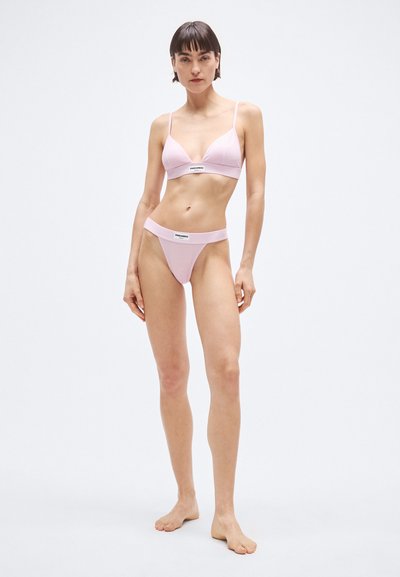 Set de lenjerie roz deschis, cu un sutien triunghiular cu bretele subțiri și tanga asortată, cu talie joasă. Materialul pare neted, cu accente de logo.