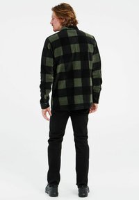 Gecarreeerd flanellen shirt in donkergroen en zwart, met kraag en een rechte snit. Gecombineerd met zwarte jeans en donkere schoenen.