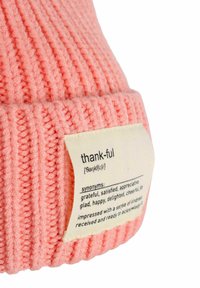 Knit beanie in soft pink with a ribbed texture. Features a fabric tag with the word "thankful" and its definition, including synonyms.