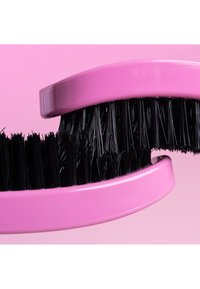 Czarna szczotka do włosów z różowym ergonomicznym uchwytem, wyposażona w gęste włosie i zakrzywiony kształt, na tle delikatnego różowego tła.