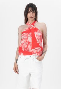 Red halter top with abstract white patterns, featuring a twisted neckline and a loose fit, paired with white shorts. Smooth fabric texture.