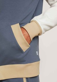 Blauwe en witte sweatshirt met een beige geribbelde manchet en zak. Zacht materiaal met een relaxed fit, dat het kleurblokontwerp en de textuur benadrukt.