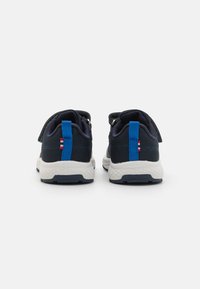 Marineblå mesh-sneakers med hvite såler, med blå stoffdetaljer og en rød-hvit-blå stripete detalj på hælen. Borrelås-stropplukking.