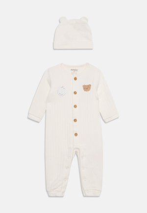 Babyrompertje in crèmekleur met bruine knopen en een patch met een teddybeer, gecombineerd met een bijpassend mutsje met kleine berenoortjes.