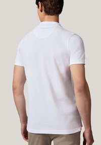 Biała krótka koszulka polo z krótkim rękawem, charakteryzująca się miękką teksturą, kołnierzykiem i subtelnym logo przy szyi. Prosty dół, elegancki fason.