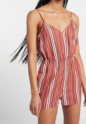 Vrouw draagt een mouwloze rode playsuit met verticale witte en zwarte strepen en een elastische tailleband.