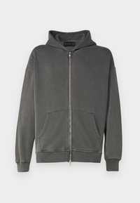 Mörkgrå zip-up hoodie tillverkad av mjukt tyg. Har en framzip, två stora framfickor och en huva med ribbad fåll och muddar.