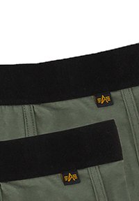 Dark green shorts with black waistband featuring a yellow logo tag. The waistband is elasticized with visible stitching details.