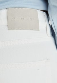Witte denim jeans met zichtbare stiksels, een slim fit, en een lichtgrijze leren label met "WE THE FREE" in reliëf op de tailleband.