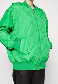 Groene gewatteerde bomberjack van glanzend synthetisch materiaal. Voorzien van een rits aan de voorkant, ribgebreide manchetten en zakken. Soepele textuur en een comfortabele pasvorm.