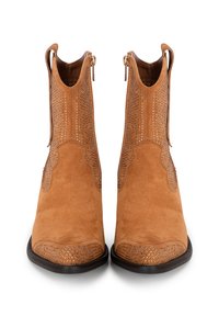 Botas de tobillo de ante marrón con perforaciones decorativas, punta redonda, cremalleras laterales y suelas lisas oscuras. Diseño clásico inspirado en el estilo western.