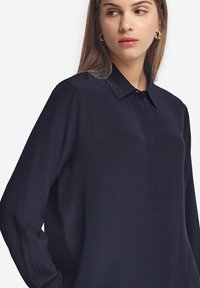 Granatowa koszula z długim rękawem, z kołnierzykiem, zapinana na guziki, o gładkiej teksturze i lekko luźnym kroju.