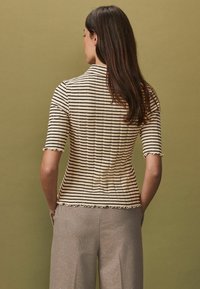 Haut à manches courtes rayé en beige et noir avec une texture côtelée, présentant des volants le long des manches et de l'ourlet. Pantalon gris.