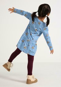 Lyseblå kjole med lange ærmer, prydet med hjorte- og blomster mønstre. Sammen med vinrøde leggings og beige snørestøvler.