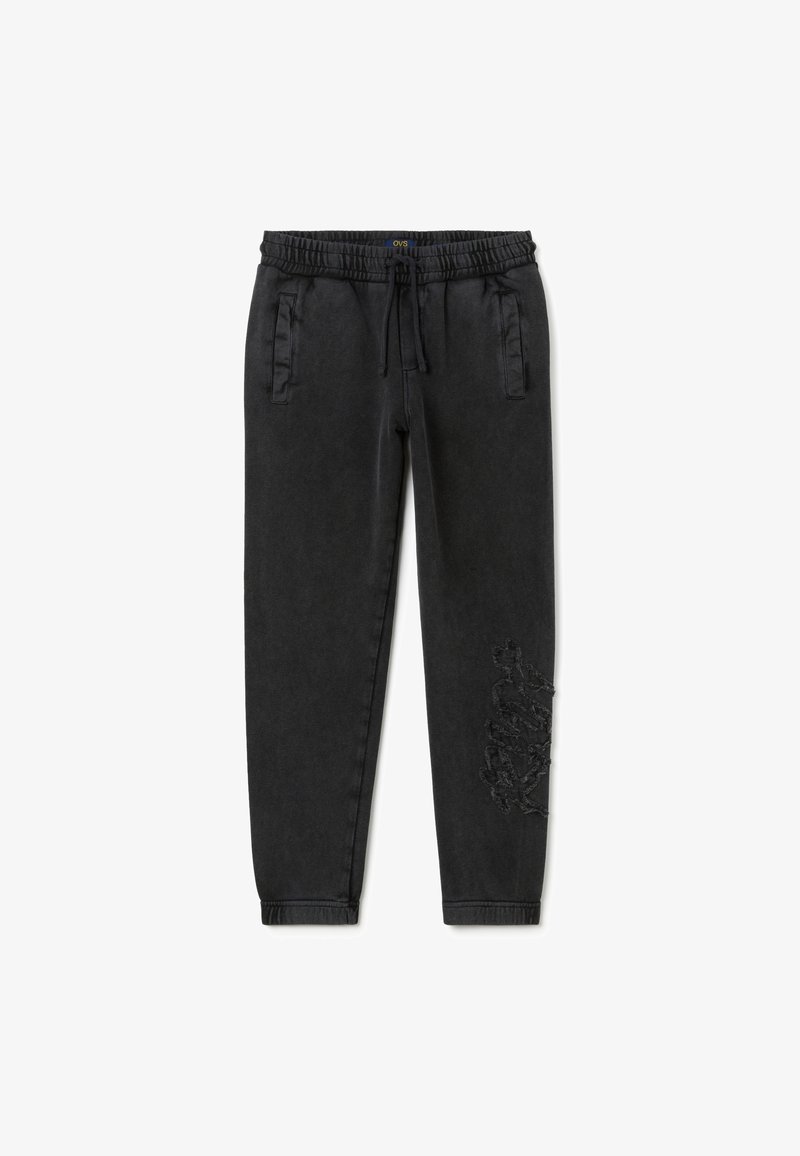 Schwarze Jogginghose aus weichem Stoff mit elastischem Bund, Seitentaschen und einem strukturierten grafischen Detail an einem Bein.