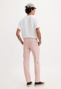 Pantaloni rosa chiaro in cotone, con un taglio dritto. Abbinati a una t-shirt bianca semplice e a scarpe da ginnastica nere.