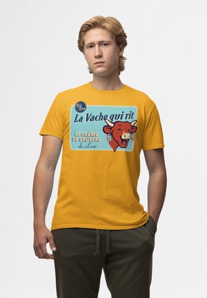 Žluté bavlněné tričko s vintage grafikou usmívající se krávy a textem "La Vache qui rit" v modrých a bílých akcent Amazon.