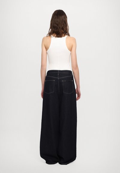 Vidde ben, mørke denimjeans med høy midje, med baklommer og kontraststing, kombinert med en hvit, tettsittende tanktopp.