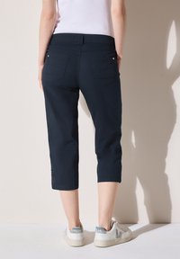 Granatowe spodnie ścięte z miękkiego materiału, z dopasowanym stanem, dwoma tylnymi kieszeniami i bocznymi akcentami. Noszone z białymi trampkami.