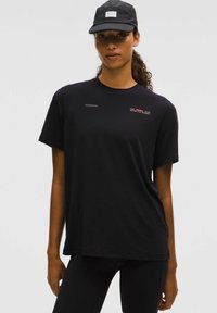 Czarna koszulka z krótkim rękawem, wykonana z miękkiego materiału, o luźnym kroju. Z przodu znajduje się napis "lululemon" oraz graficzny tekst w kolorze czerwonym i białym.