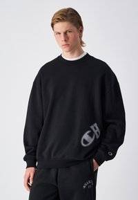Sweatshirt noir surdimensionné en mélange de coton, avec un col côtelé et un grand logo en bas à gauche à l'avant. Texture lisse.