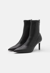 Schwarze Lederstiefeletten mit spitz zulaufender Schuhspitze, Reißverschluss an der Rückseite und schlankem hohen Absatz. Glatte Textur mit minimalen Designdetails.