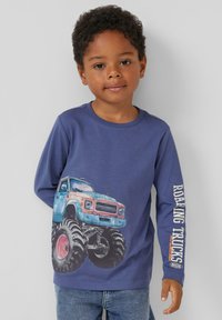 Niebieska koszula z długim rękawem z dużym nadrukiem przedstawiającym monster truck oraz napisem "ROARING TRUCKS" na rękawie. Bawełnowy materiał, luźny krój.