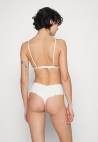 Ensemble de lingerie rose clair comprenant un bralette à fines bretelles et une culotte blanche à bords festonnés avec une texture douce. Fermeture à l'arrière réglable.