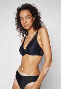 Black lace bra with floral pattern, plunging neckline, wide straps, and soft fabric. Paired with black bikini briefs, smooth texture.