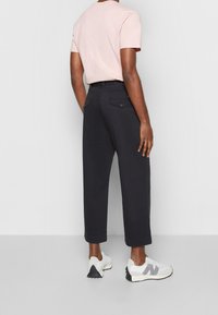 Pantalones cortos negros con bolsillos traseros abotonados, combinados con una camiseta de manga corta rosa claro y zapatillas blancas con detalles grises.