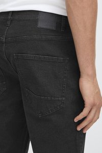 Černé džínové kalhoty z denimu mají klasický design s pěti kapsami, hladkou texturu a jemné vybledlé akcenty. Součástí je také černá kožená záplata.