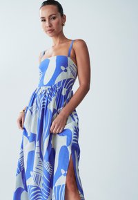 Sininen ja valkoinen kuvioitu mekko, jossa on istuva olkaimeton yläosa, virtaava hame ja sivuaukko. Valmistettu kevyestä kankaasta, jolla on sileä rakenne.