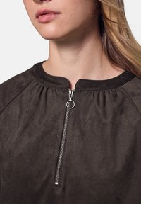 Sort zip-op toppen lavet af blød, struktureret stof med rund halsudskæring og samlet detaljering omkring kraven. Sølv lynlås hardware accent.