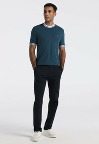 Teal korte mouwen polo shirt met witte kraag en accenten op de mouwen, gecombineerd met donkere broek en witte sneakers. Glad materiaal met minimale details.