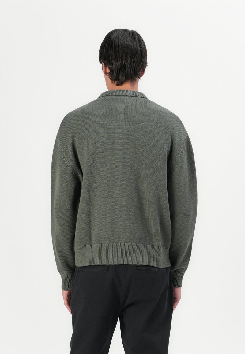 Green knitted sweater with a ribbed hem and cuffs, featuring a collar and a classic fit. The texture appears soft and comfortable.