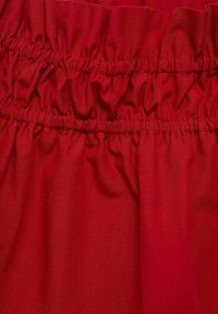 Tessuto rosso con fasce elastiche arricciate che creano texture. Superficie liscia, peso medio, colorazione uniforme senza motivi o decorazioni.