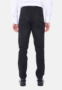 Chinos neri in cotone con una vestibilità slim, dotati di tasche posteriori e dettagli di cucitura discreti. Indossati con una camicia bianca a maniche lunghe e scarpe nere lucide.