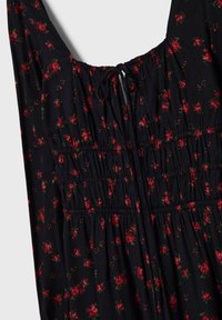 Robe noire à petits motifs floraux rouges, corsage froncé et détail noué au niveau de l'encolure.