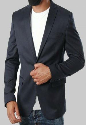 Blazer bleu marine en tissu lisse, doté d'un bouton simple, de revers crantés et d'une poche frontale, porté sur une chemise blanche.