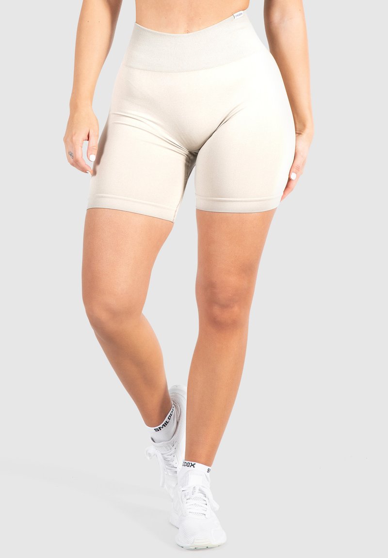 Beige hoge taille fietsbroek met een gladde textuur, tot halverwege de dij lengte en een geribbelde tailleband. Gecombineerd met witte sportschoenen.