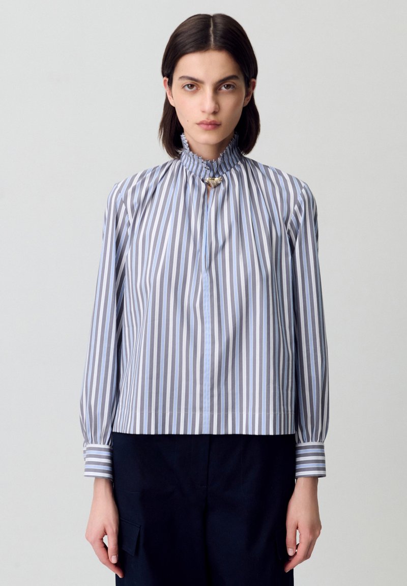 Blusa a rayas en azul claro y gris, con un alto cuello con volante, mangas largas abullonadas y un acento dorado en el escote.