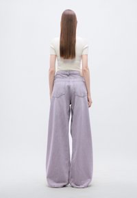 Φαρδιά τζιν σε ανοιχτό μωβ χρώμα με ψηλή μέση, δύο πίσω τσέπες και απαλή υφή denim. Συνδυασμένα με εφαρμοστό κρεμ τοπ, από πίσω.