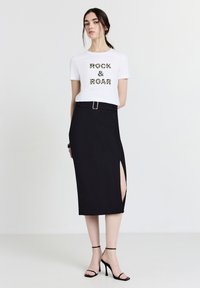 Weißes Baumwoll-T-Shirt mit "ROCK & ROAR" im Leopardenmuster. Schwarzer Midirock mit seitlichem Schlitz und Gürtel; kombiniert mit schwarzen Riemchenschuhen.